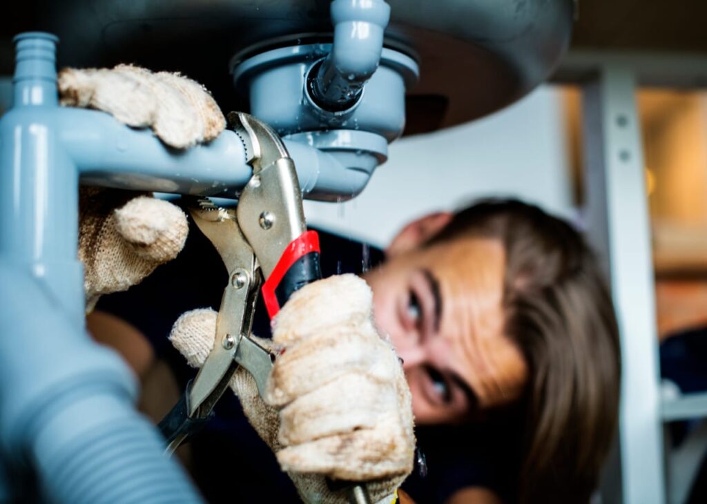Plumber using pliers to repair sink pipes in residential plumbing services.