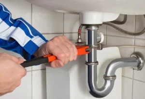 Residential plumbing repair under sink using wrench on pipe connection.