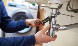 Residential plumbing care with technician tightening under-sink pipe connection.