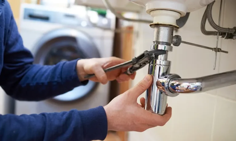 Residential plumbing care with technician tightening under-sink pipe connection.