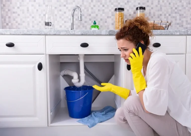 Homeowner dealing with residential plumbing problems from leaking under-sink pipe.